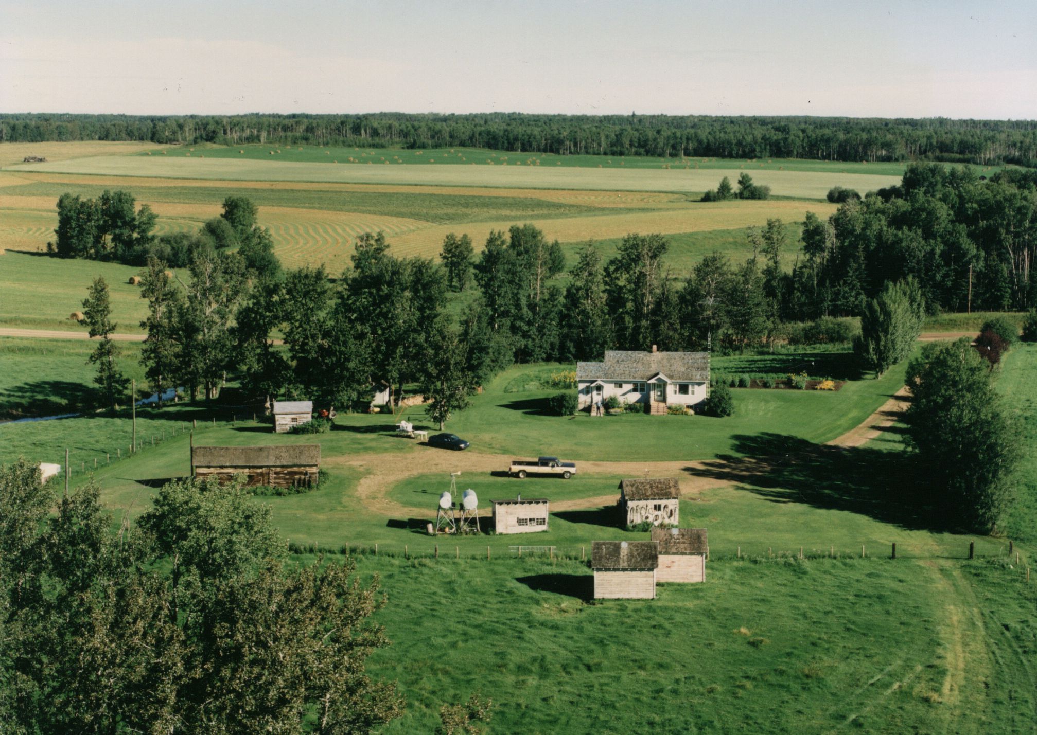 Aerial photo looking south. Mikaluks' field across the road in background. Note water in creek. Cattle shed, corral and pens off-photo some distance to the left. Circa 1996. Aerial photo looking south. Mikaluks' field across the road in background. Note water in creek. Cattle shed, corral and pens off-photo some distance to the left. Circa 1996.